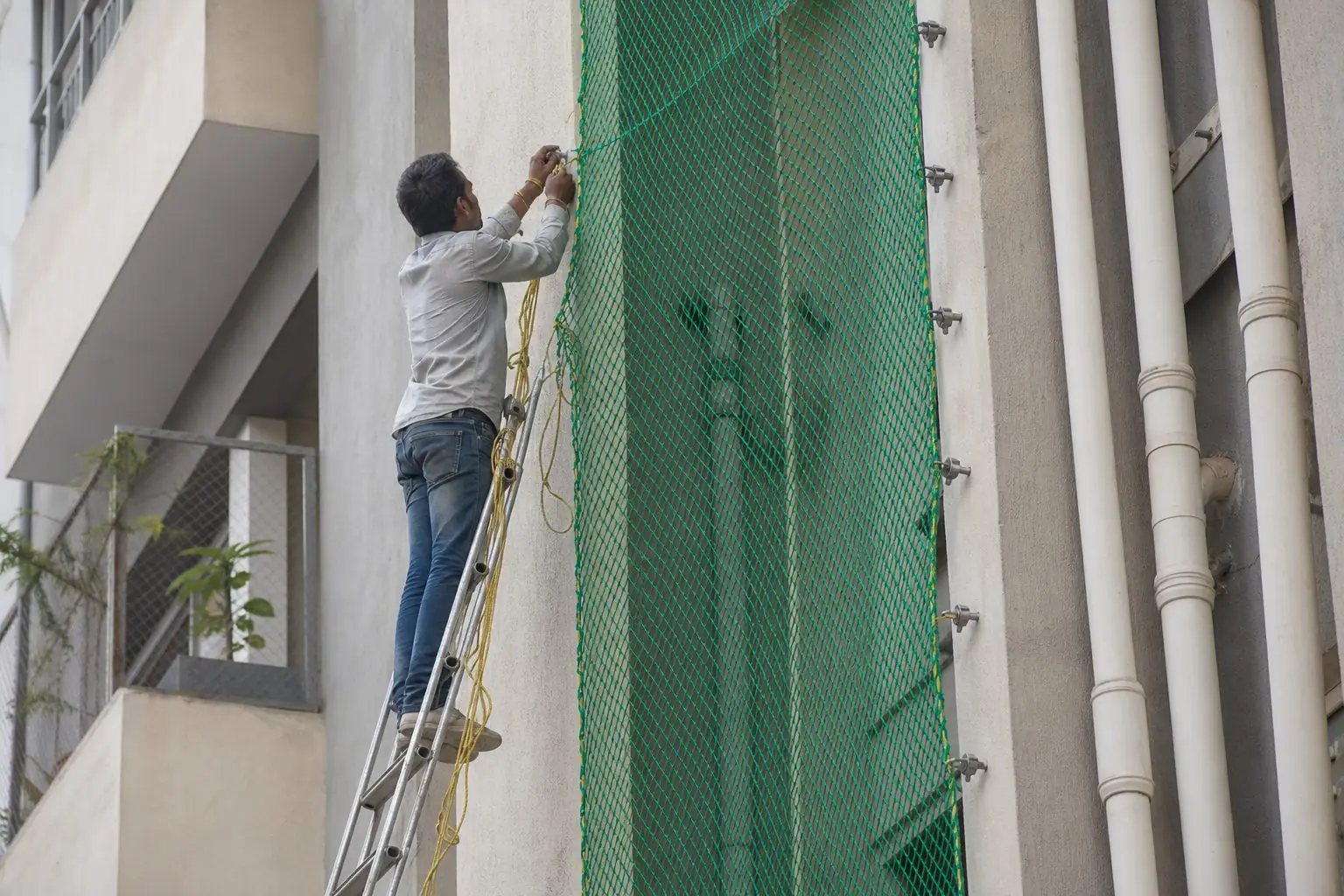 During outside vertical duct safety net installation with technician fixing green net in Hyderabad